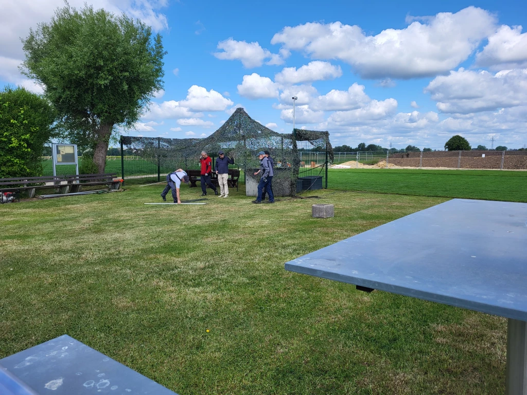 Mehrere Personen bei Gartenarbeiten auf Rasenfl&auml;che, Camouflage-Zelt, Baum, bew&ouml;lkter Himmel
