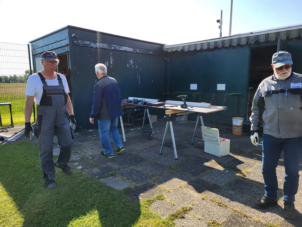 Zwei M&auml;nner in Arbeitskleidung an Werkbank vor Metallcontainer, Arbeitsutensilien, Werkzeuge und Rasenfl&auml;che
