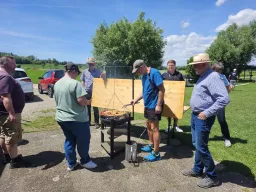 Mehrere Teilnehmer stehen um den Grill, auf dem Rost liegen Fleisch und Gemüse