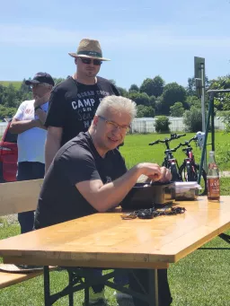 Ein Teilnehmer arbeitet am Biertisch an Modellbauteilen, zwei Männer schauen ihm dabei zu