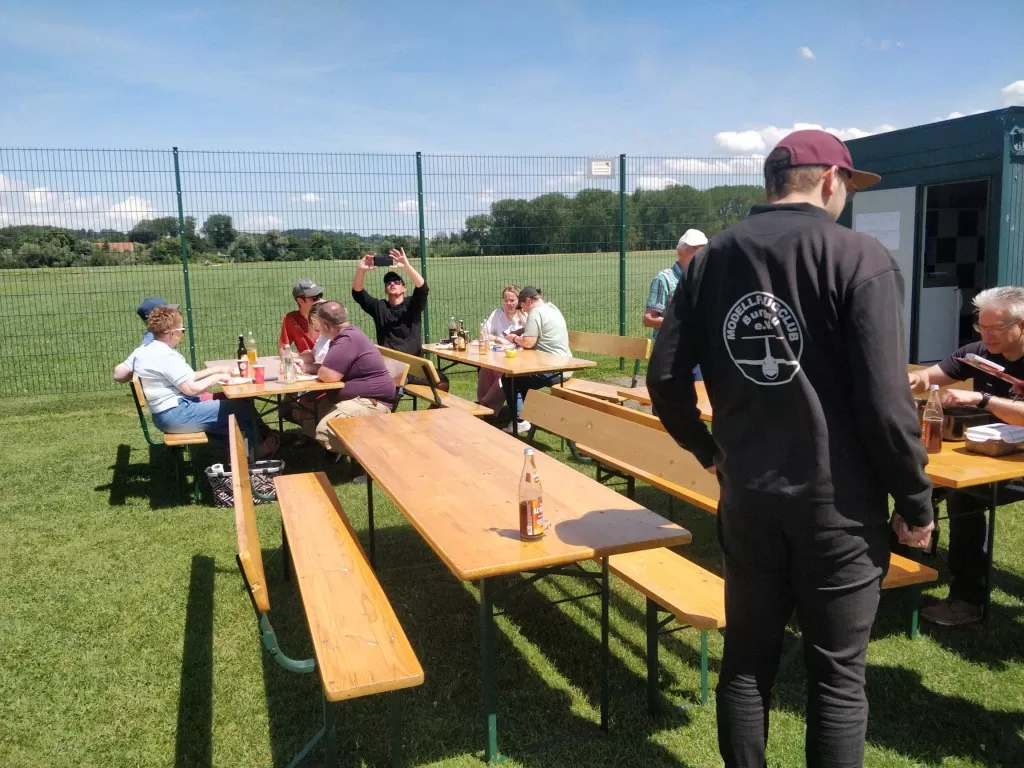 Teilnehmer sitzen beim gemeinsamen Mittagessen an Biertischen vor dem Vereinsheim