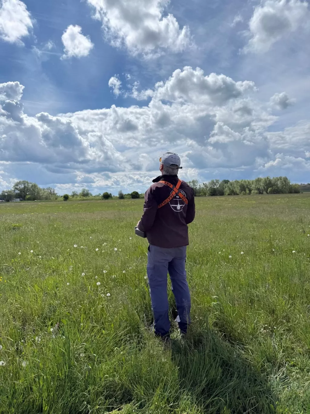 Pilot steht in der hohen Wiese und verfolgt sein Modell am bewölkten Himmel