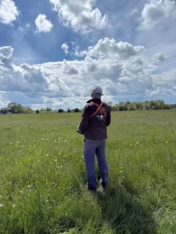 Pilot steht in der hohen Wiese und verfolgt sein Modell am bewölkten Himmel