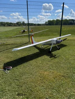 Weißes Motormodell auf der Wiese, im Hintergrund ein Segelflugmodell auf der Startbahn