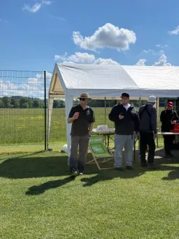 Teilnehmer stehen mit Getränken am Pavillon, davor ein Liegestuhl im Gras