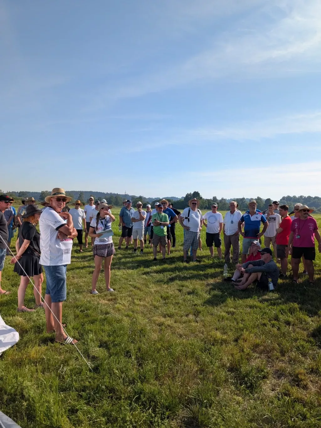 Große Gruppe von Teilnehmern beim Briefing auf der Wiese, eine Helferin verliest Informationen