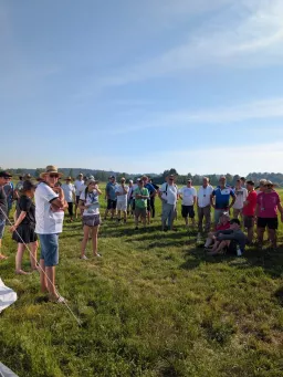 Große Gruppe von Teilnehmern beim Briefing auf der Wiese, eine Helferin verliest Informationen