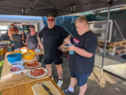 Helfer belegen Pizzen an der Vorbereitungsstation, rechts der Pizzaofen