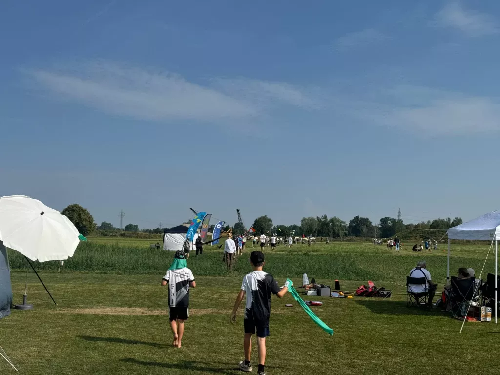 Zwei Jugendliche gehen mit einem Windband über das Gelände, im Hintergrund Fahnen und Pavillons