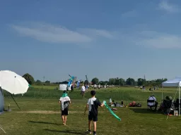 Zwei Jugendliche gehen mit einem Windband über das Gelände, im Hintergrund Fahnen und Pavillons