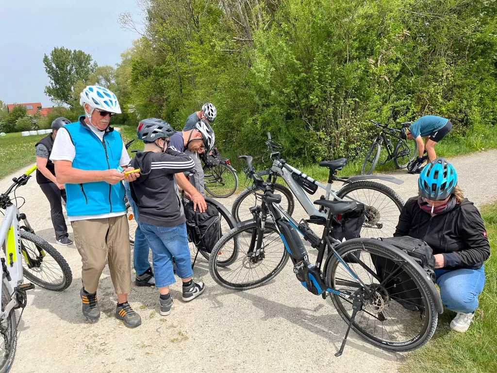 Fünf Radfahrer mit E-Bikes machen Pause auf einem Schotterweg, umgeben von Bäumen und Grünfläche