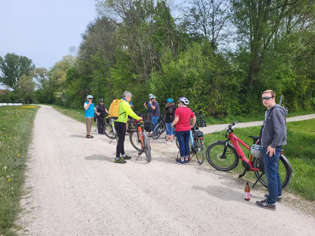 Mehrere Radfahrer mit Fahrrädern auf einem Schotterweg, umgeben von grüner Frühlingslandschaft mit Bäumen und Wiesen