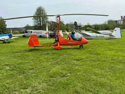 Orangefarbener Gyrocopter-Modell mit blau-weißem Segelflugzeug auf grüner Rasenfläche beim Oktoberfest-Event