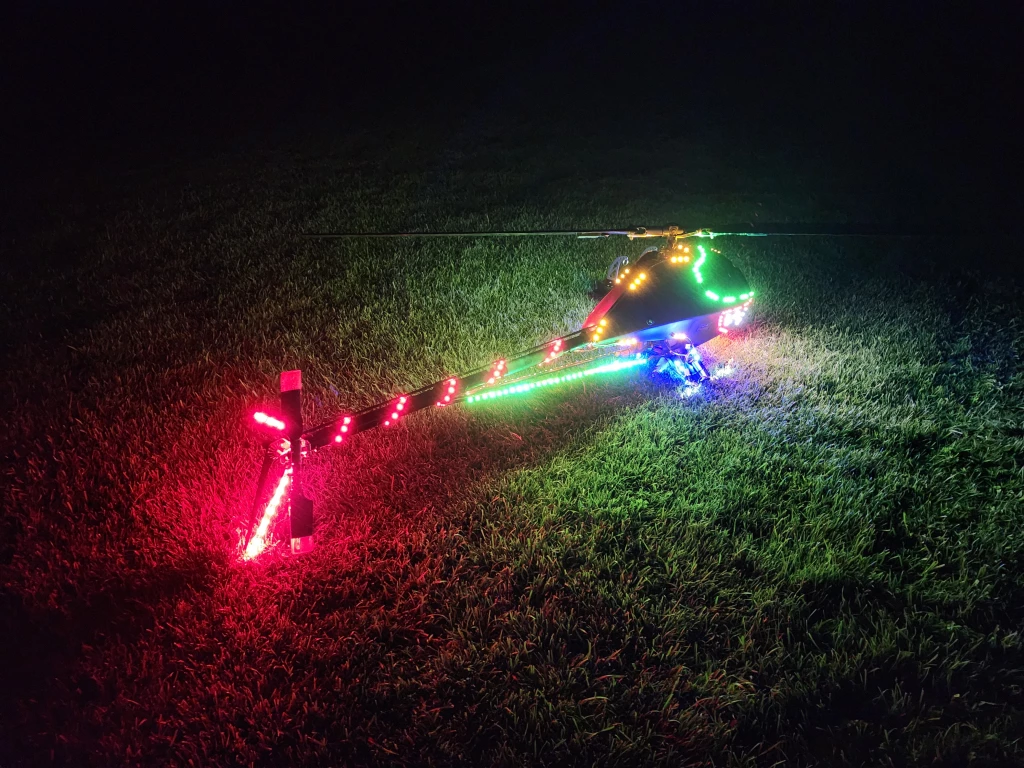 Nachtaufnahme eines Modellhubschraubers mit bunten LED-Beleuchtungen in Gr&uuml;n, Rot und Blau auf Rasenplatz