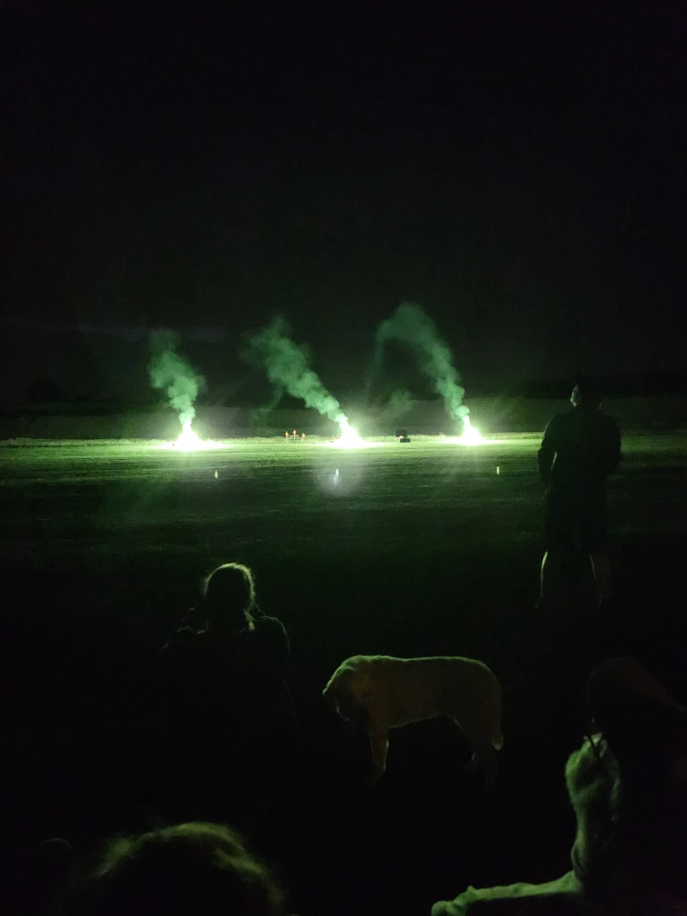 Drei gr&uuml;n leuchtende Rauchs&auml;ulen auf dunklem Nachtplatz, Silhouetten von Zuschauern im Vordergrund, Modellflug-Nachtveranstaltung