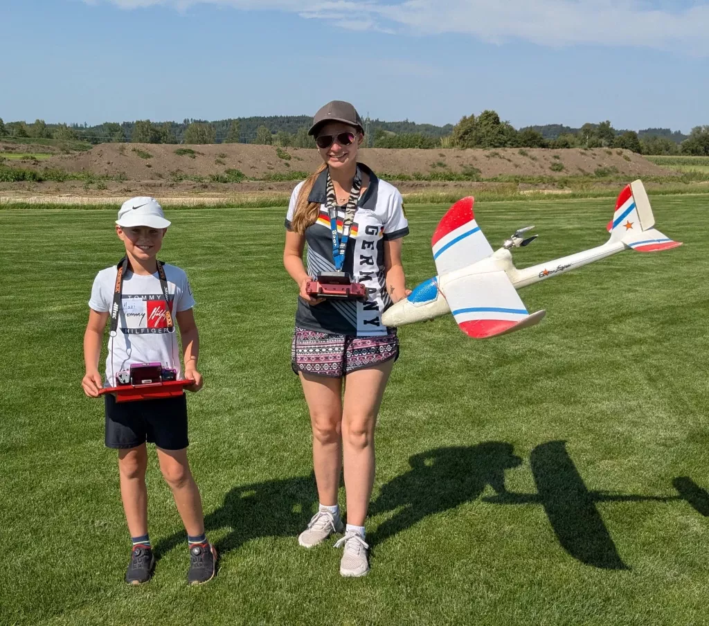 Zwei junge Modellflieger mit Flugmodellen auf Vereinsgelände, grüne Wiese, Sommertag