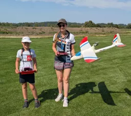 Zwei junge Modellflieger mit Flugmodellen auf Vereinsgelände, grüne Wiese, Sommertag
