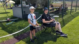 Zwei Personen am Modellflugplatz: Jugendlicher und Erwachsener mit Fernsteuerung, Modellflugzeug, grüne Rasenfläche