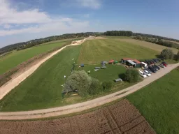 Luftaufnahme eines Modellfluggeländes mit grünen Wiesen, Parkplatz, Vereinscontainern und Flugfeld