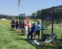 Gruppe von Menschen an einem sonnigen Tag auf einem Modellflugplatz, stehen entlang eines grünen Rasens, Zaun im Hintergrund