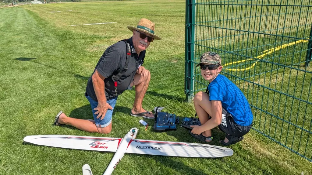 Zwei Personen mit Modellflugzeug auf Rasenplatz: Älterer Mann und Kind richten Segelflugmodell von Multiplex her