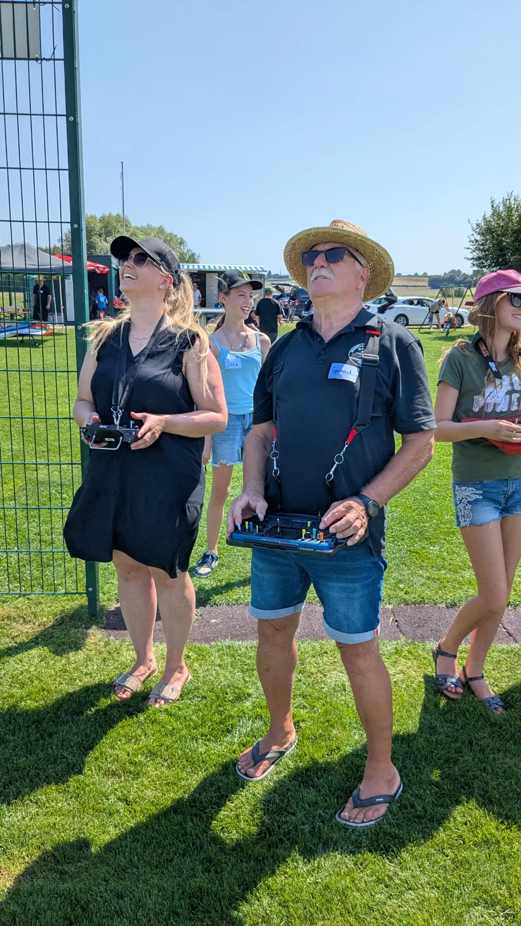 Zwei Personen mit Fernbedienungen auf Rasenfl&auml;che, Sommertag, Zaun im Hintergrund, Mann mit Strohhut und Sonnenbrille