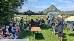 Gruppe von Menschen unter Sonnenschirmen auf Rasenfläche, Berglandschaft im Hintergrund, Modellflug-Veranstaltung