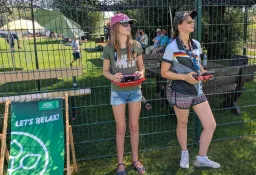Zwei junge Frauen mit Fernsteuerungen an einem Modellflug-Event, AOK-Banner 'Let's relax', Zeltgelände im Hintergrund