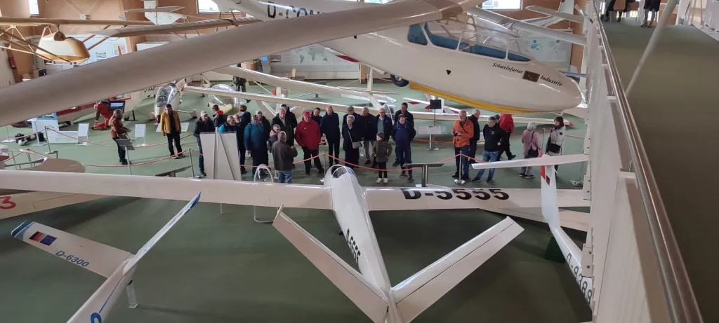 Mehrere weiße Segelflugzeugmodelle in einem Ausstellungsraum mit Besuchergruppe und Absperrungen