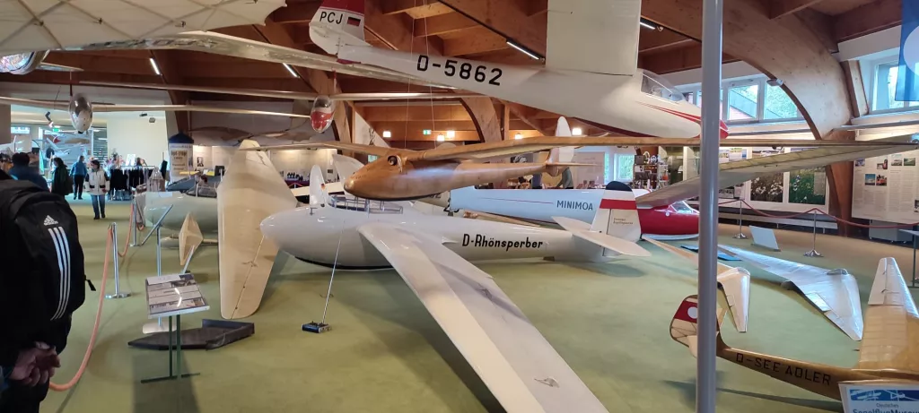 Mehrere historische Segelflugzeugmodelle in einem Ausstellungsraum, darunter ein weißes Flugzeug mit Kennzeichen D-Rhönsperber und weitere Modelle an Aufhängungen