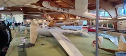 Mehrere historische Segelflugzeugmodelle in einem Ausstellungsraum, darunter ein weißes Flugzeug mit Kennzeichen D-Rhönsperber und weitere Modelle an Aufhängungen