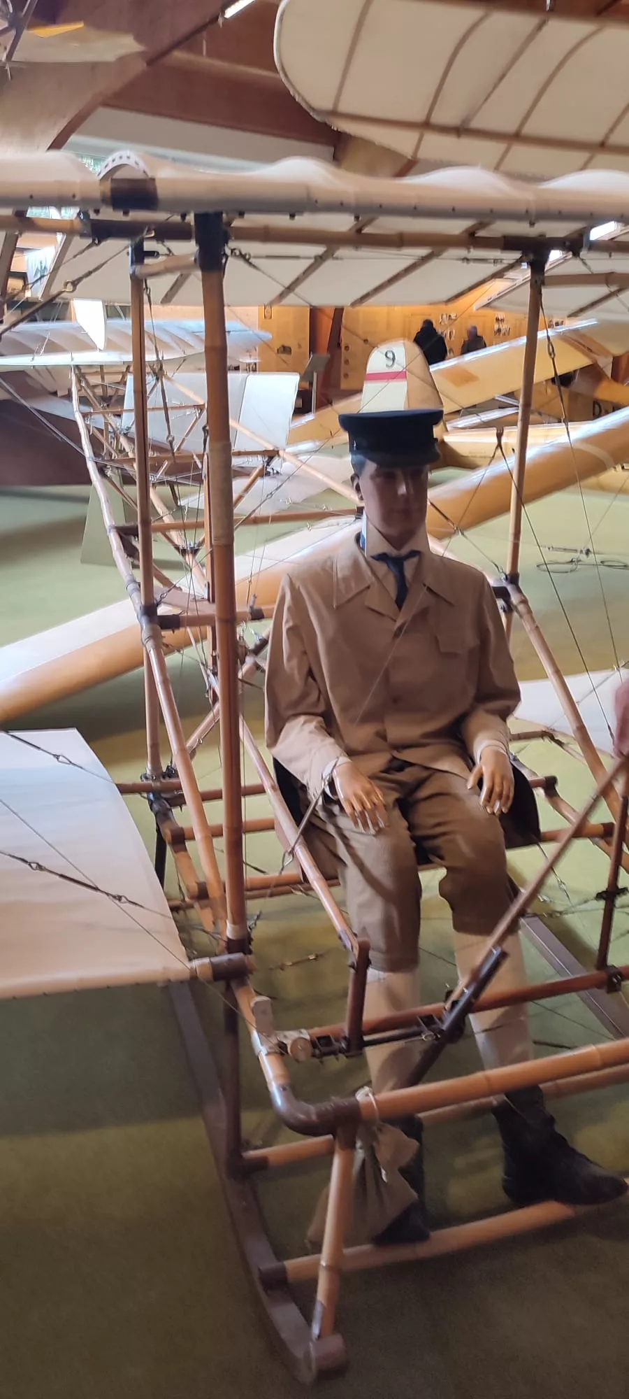 Museale Ausstellung eines historischen Flugzeugs mit Mannequin in Piloten-Uniform, Holzgestell und Flügel im Hintergrund