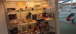 Glasvitrine mit verschiedenen alten elektronischen Geräten, Messgeräten und Schaltkreisen, im Hintergrund ein Modellflugzeug