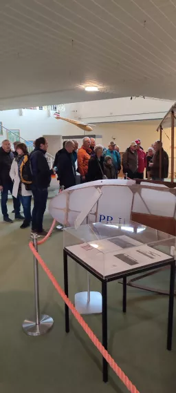 Gruppe von Besuchern in Ausstellungsraum, im Vordergrund Modellflugzeug-Vitrine mit Absperrung