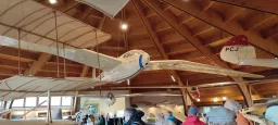 Hölzerner Museumsraum mit historischen Modellflugzeugen, Segelflugzeug Reimar III hängt von Decke, Besucher im Vordergrund