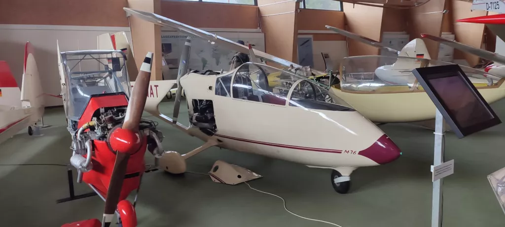 Weiß-rotes Segelflugmodell M76 mit Propellerflugzeug in Ausstellungsraum, mehrere Flugzeugmodelle im Hintergrund