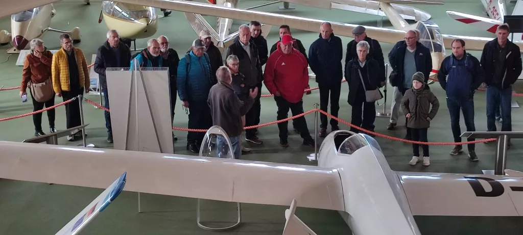 Gruppe von Männern und einer Frau in Winterkleidung neben historischen Segelflugzeugen in einer Ausstellungshalle