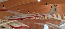Weißes und rotes Segelflugmodell vom Typ DM-2704 mit Kennzeichen, in Holzhalle ausgestellt, hängt an Decke