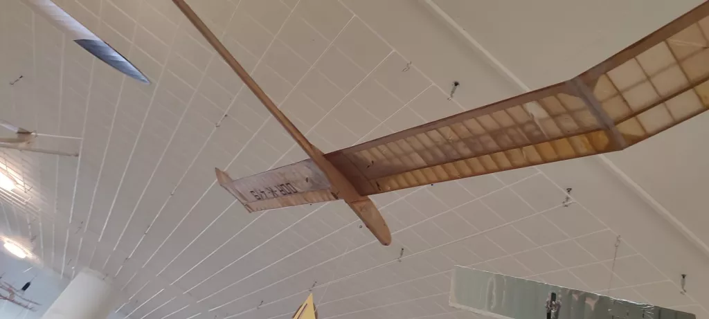 Holz-Segelflugmodell mit Gitterstruktur, von der Decke einer hellen Ausstellungshalle hängend