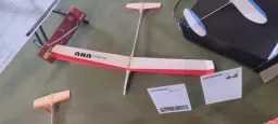 Holz-Modellflugzeug in rot-weiß mit Bauanleitungsblättern auf grünem Untergrund, mehrere Flugzeugteile