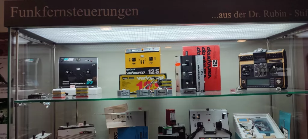 Vitrine mit verschiedenen alten Funkfernsteuerungen für Modellflugzeuge, in unterschiedlichen Farben und Designs aus den 1970er/80er Jahren