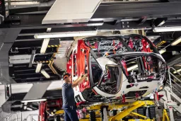 Weißer Hubschrauber-Rumpf in Montagestation, Arbeiter steht daneben und arbeitet an Flugzeugkomponenten