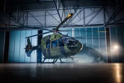 Grün-getarnter Militärhubschrauber vom Typ H145M in geöffnetem Hangar mit Nebel und Industriebeleuchtung