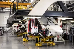 Weißer Helikopter in Fertigungshalle auf gelben Montagebühnen, umgeben von Produktionseinrichtungen und Kränen