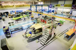 Blick in eine große Industriehalle mit Hubschraubern in verschiedenen Montagestadien, Arbeitsplattformen und Produktionseinrichtungen