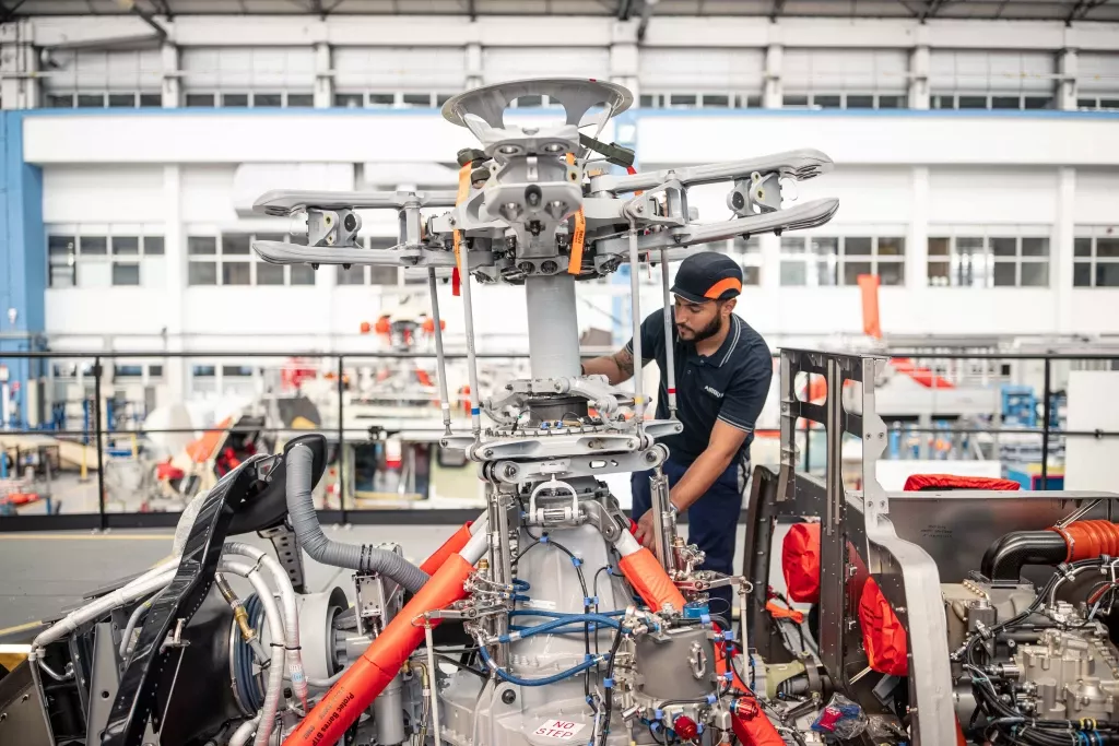 Techniker arbeitet an komplexer Helikopter-Rotorkonstruktion in moderner Industriehalle mit Metallstrukturen
