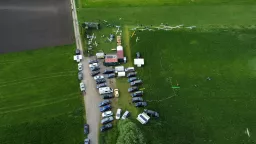 Luftaufnahme eines Modellflugplatzes mit mehreren weißen Segelflugmodellen auf grüner Wiese, Autos auf Schotterweg, Vereinsgelände mit Gebäuden