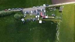 Luftaufnahme eines Modellflugplatzes mit mehreren weißen Segelflugmodellen und zahlreichen Autos auf Grünfläche