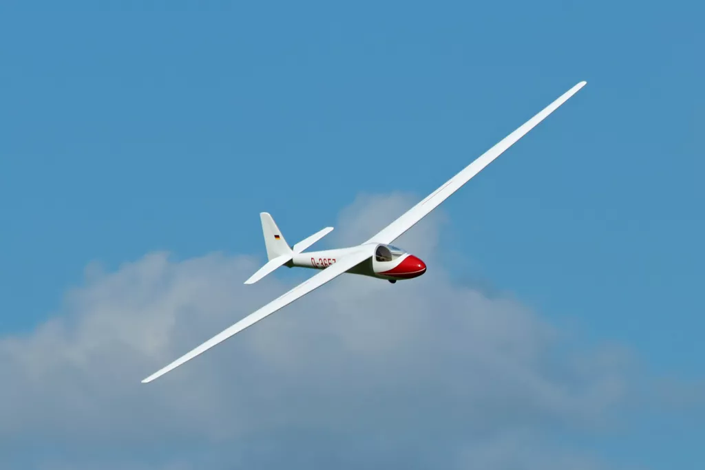 Wei&szlig;es Segelflugzeug mit roter Nase fliegt vor wolkigem Himmel, Deutscher Kennzeichnung sichtbar