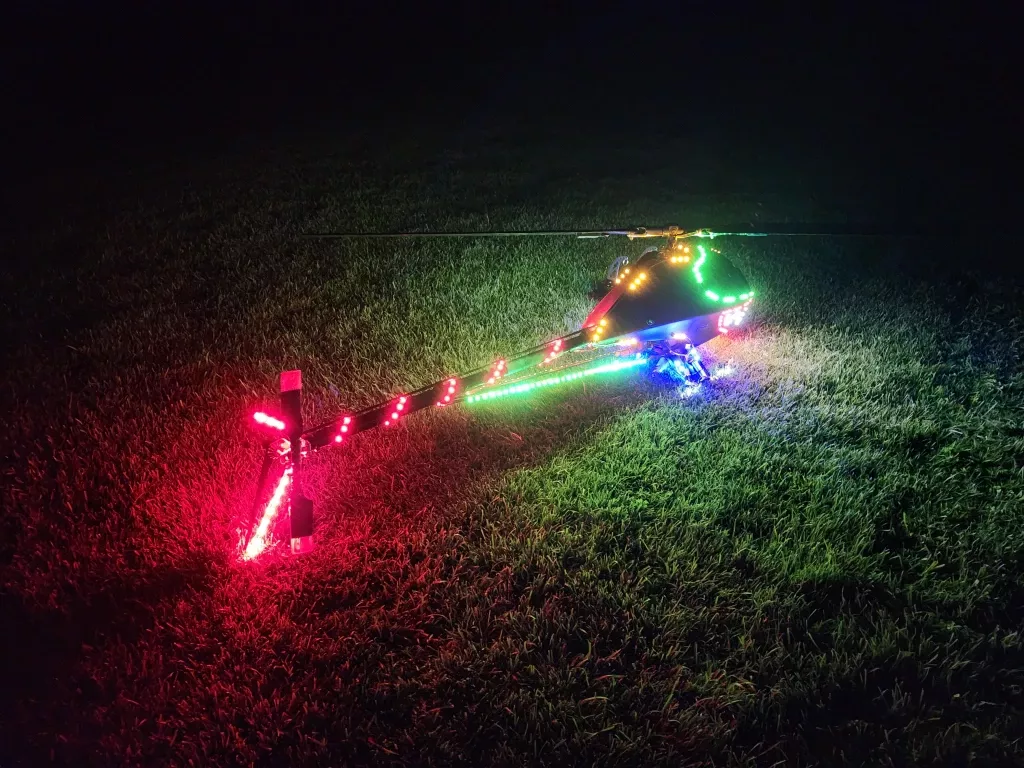 Modellhubschrauber mit bunten LED-Lichtern in Gr&uuml;n, Rot und Blau auf Grasnarbe bei Dunkelheit
